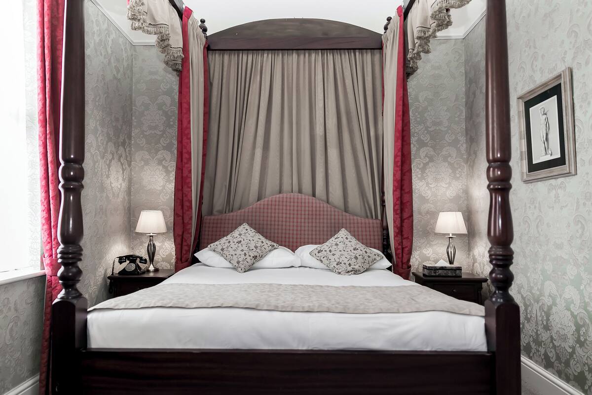 A four-poster bed with a canopy, two bedside tables with lamps, and a framed picture on the wall.