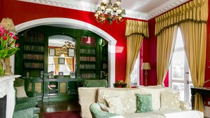 A room with a red wall, a green archway leading to a library, a beige sofa, and a chandelier. - Butlers Townhouse (Dublin)