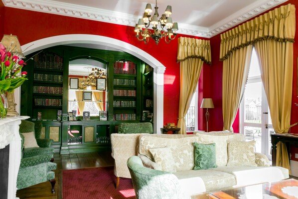 A room with a red wall, a green archway leading to a library, a beige sofa, and a chandelier. - Butlers Townhouse (Dublin)