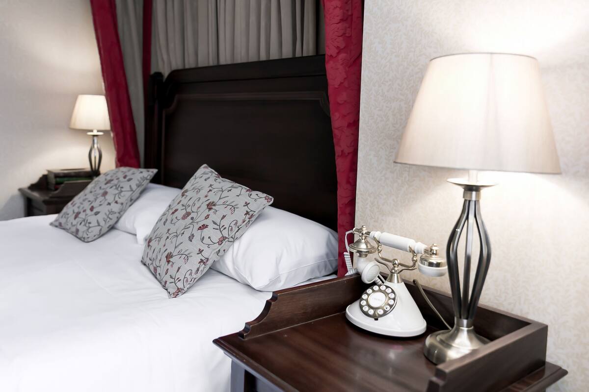 A neatly made bed with floral pillows, a classic rotary phone on a bedside table, and a lamp.