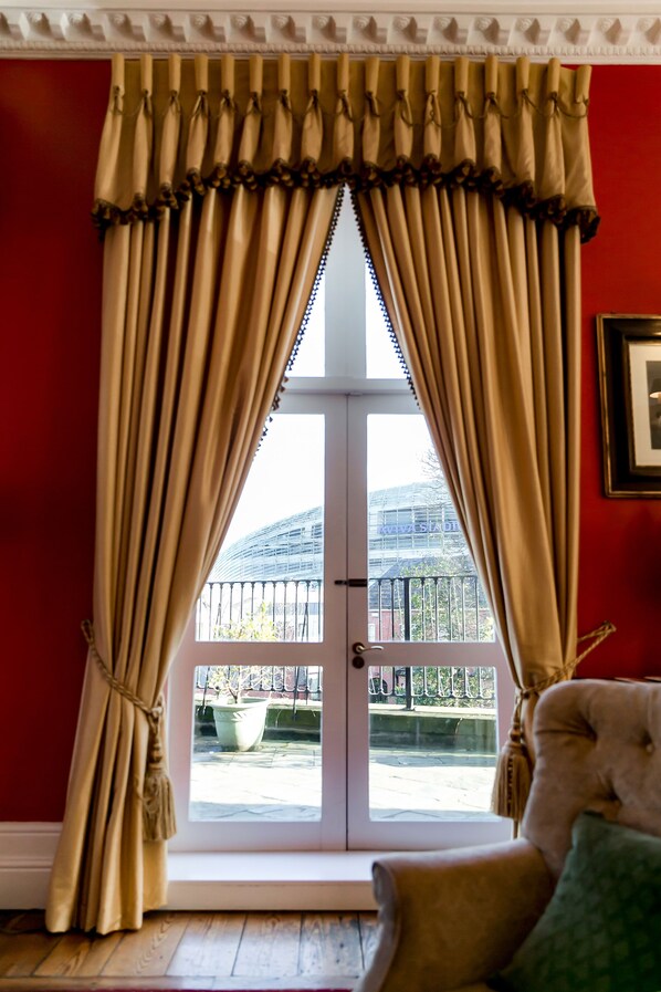 Une pièce dotée d’une grande fenêtre, de rideaux beiges, d’une porte blanche et donnant sur un espace extérieur avec un bâtiment et une clôture.