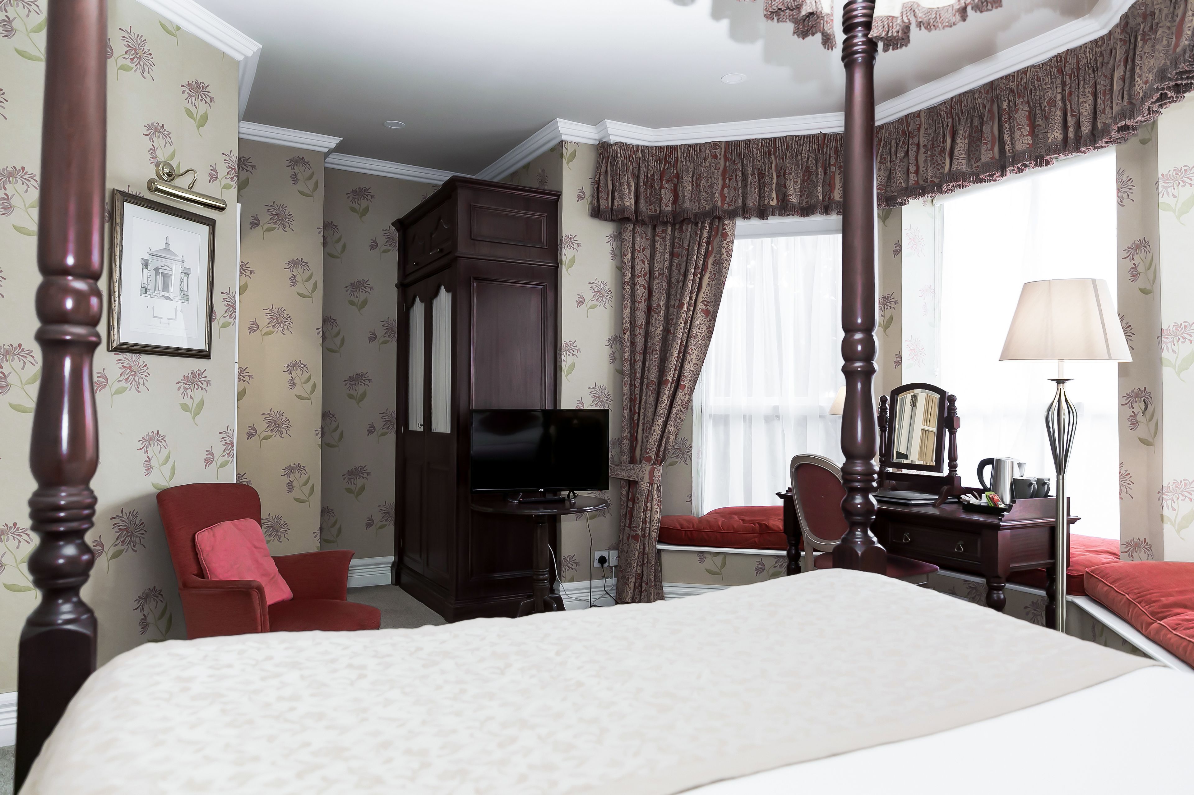 A bedroom with a large bed, a television, a desk with a lamp, a chair, and a wardrobe.