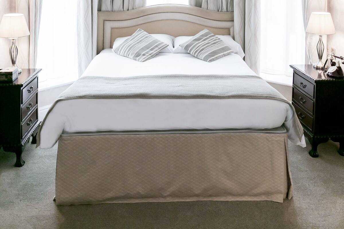 A neatly arranged bedroom with a large bed, two bedside tables with lamps, and a window with curtains.