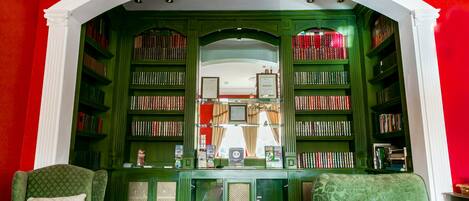 A library with green bookshelves, two green armchairs, and a glass display case.