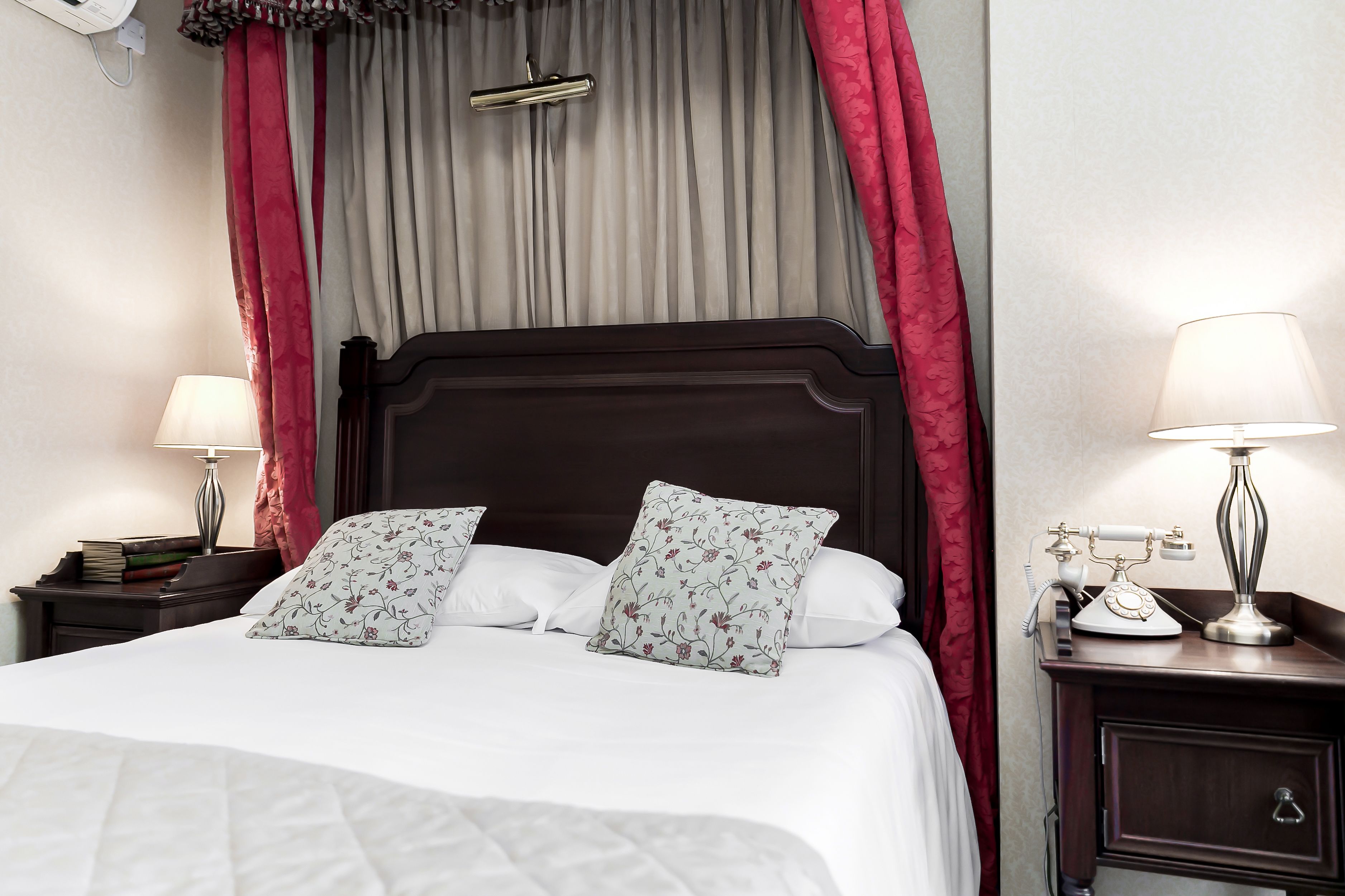 A neatly made bed with floral pillows, a dark wooden headboard, and a nightstand with a lamp and books.