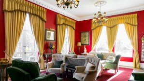 A room with red walls, large windows with yellow curtains, and multiple seating areas including green and beige armchairs. - Butlers Townhouse (Dublin)