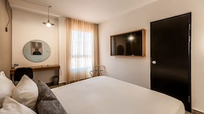 A hotel room with a bed, a desk, a chair, a round mirror, a TV, and a door.