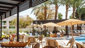 An outdoor pool area with lounge chairs, umbrellas, and a dining setup with a fruit bowl. - Jacob Eilat (Eilat)