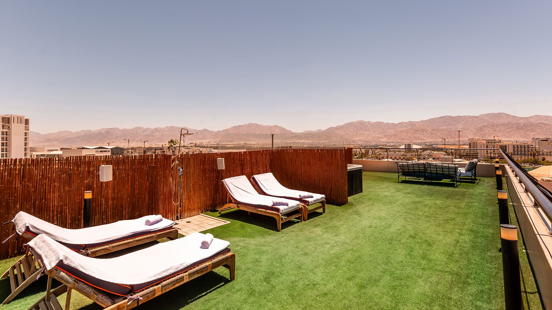 A rooftop terrace with two sun loungers, a small table, and a view of mountains.