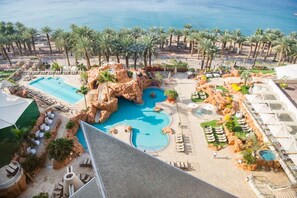 A resort with multiple pools, palm trees, and a view of the sea.