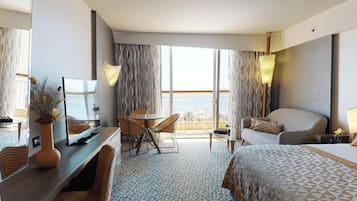 A hotel room with a bed, a desk with a TV, a chair, a sofa, and a balcony with curtains.