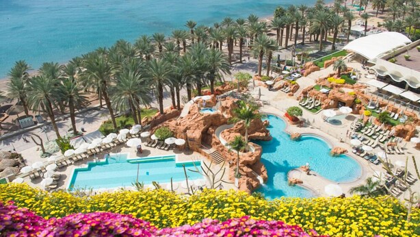 Een resort met een groot zwembad, palmbomen en een strandgebied.