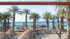 Uitzicht op het strand met palmbomen, strandparasols en helder zicht op zee.