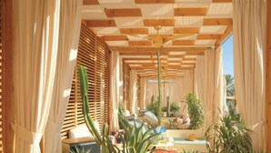 Een gang met houten lambrisering en gordijnen, die uitkomt in een zithoek met planten en een tafel.