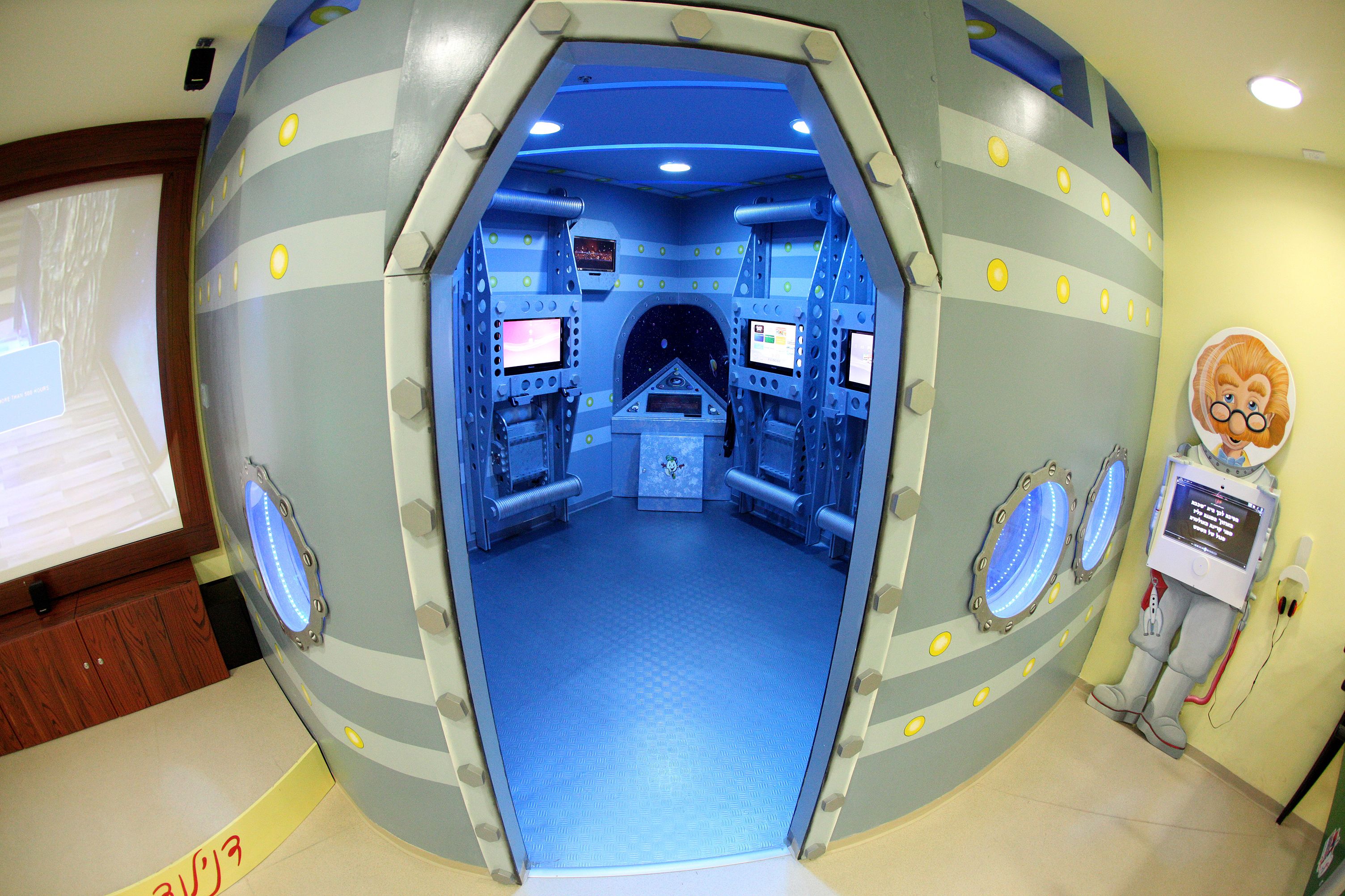 A room with a futuristic design, featuring a central control panel, multiple monitors, and a blue floor.