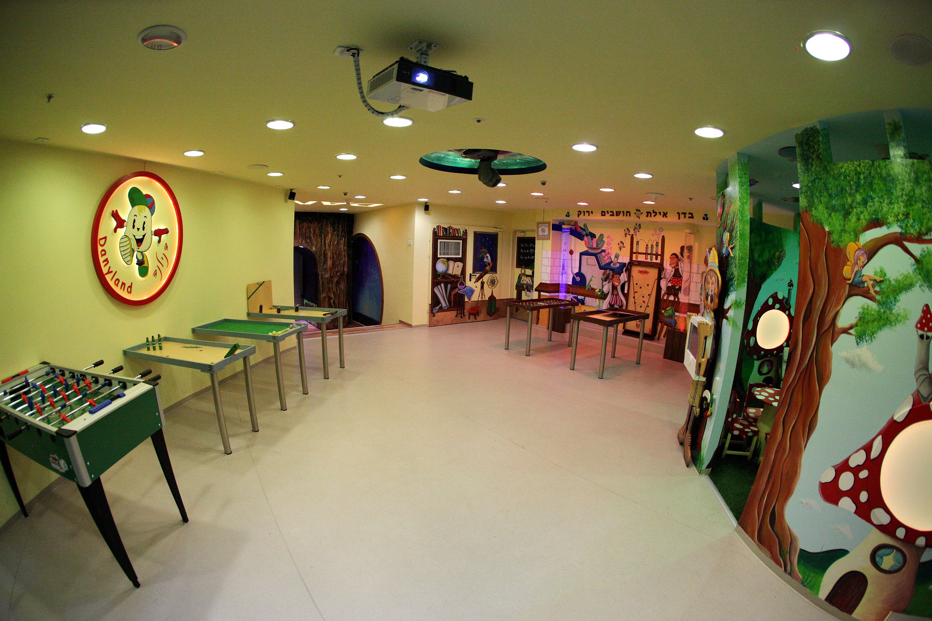 A room with a foosball table, a table tennis table, and a projection screen.