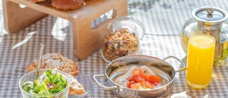 A breakfast setup with bread, pastries, cheese, fruits, and a glass of orange juice on a checkered tablecloth.