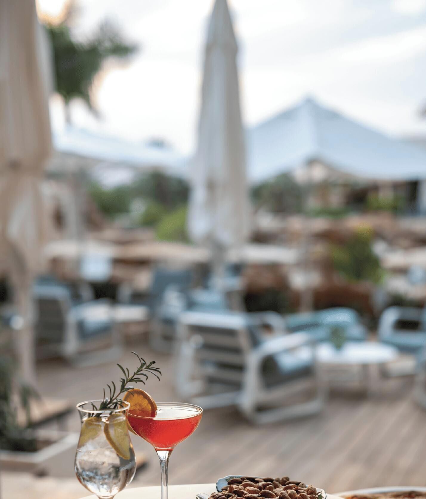 Ein Cocktailglas mit Garnitur, eine Flasche mit Zweig und eine Schale Nüsse auf einem Holzboden.