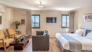 Ein Hotelzimmer mit Bett, Sofa, Couchtisch, Fernseher und Fenster mit Blick auf die Stadt.