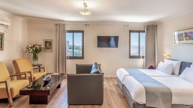 Une chambre d’hôtel avec un lit, un canapé, une table basse, une télévision et une fenêtre donnant sur la ville.