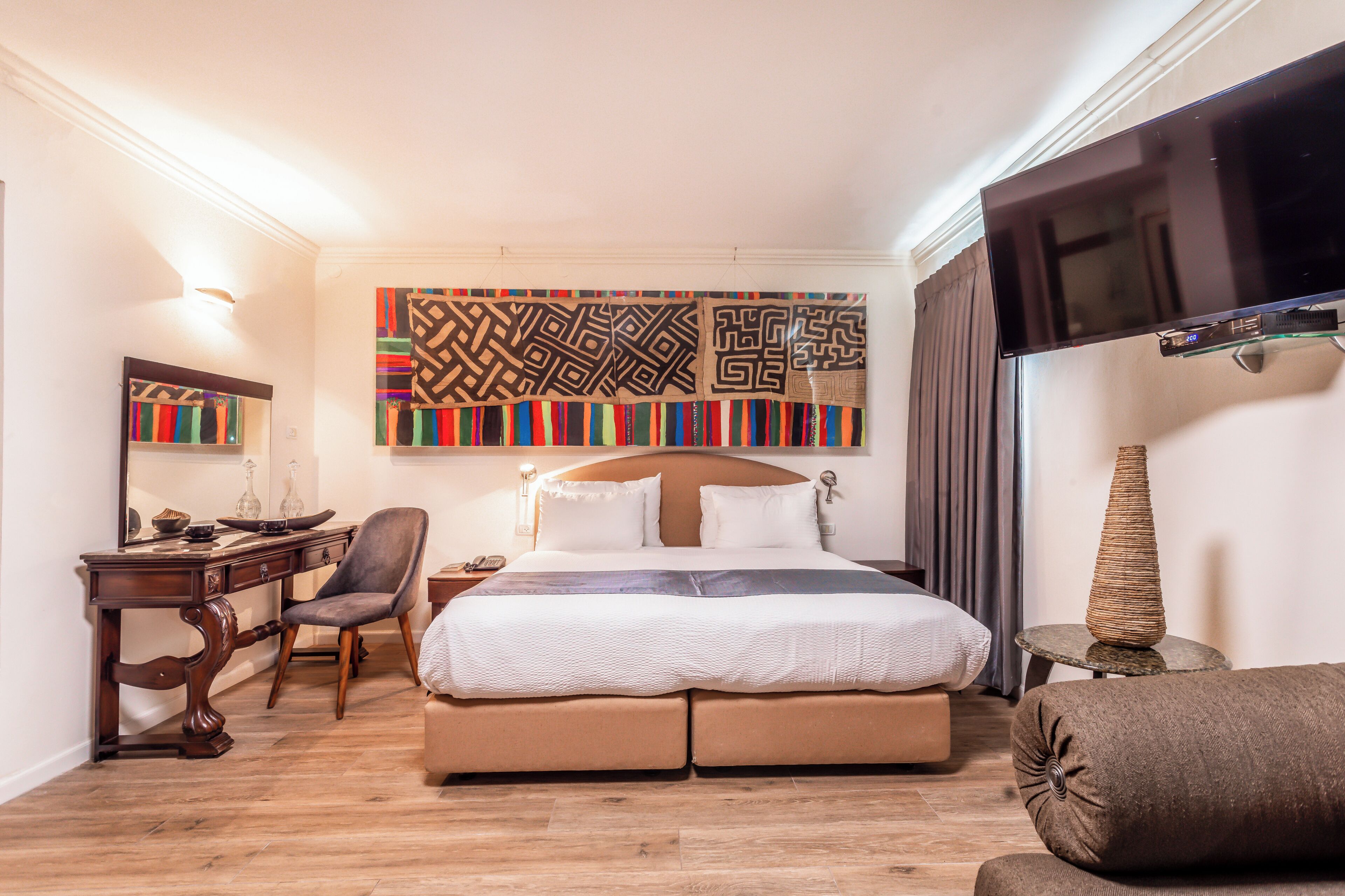 A hotel room with a bed, a desk, a chair, a television, and a decorative wall hanging.