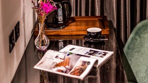 Une table en bois sur laquelle se trouvent un vase de fleurs, une machine à café, une tasse et un magazine.