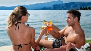 Dos personas sentadas junto a un lago, con montañas al fondo.