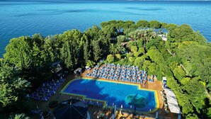 Vista aérea de un resort con una gran piscina rodeada de exuberante vegetación y una vista despejada del mar.