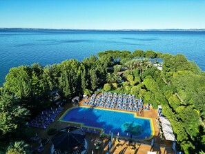 Vista aérea de um resort com uma grande piscina, cercada por vegetação exuberante e uma vista clara do mar.