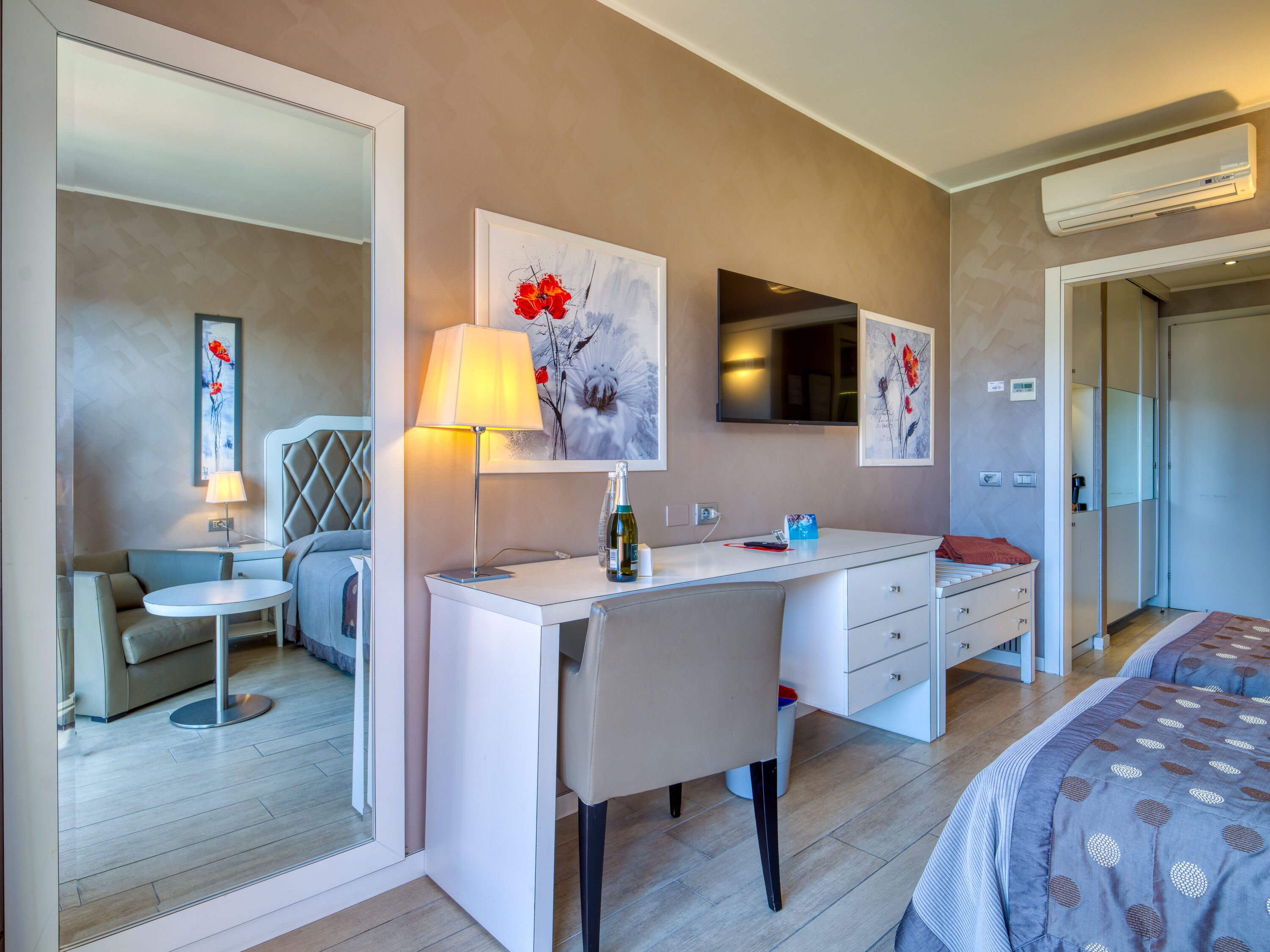 A modern hotel room with a desk, chair, and a bed with a patterned duvet.