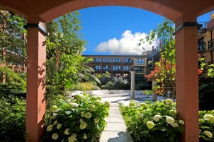 Un patio con un camino que lleva a un edificio, rodeado de follaje y flores blancas.
