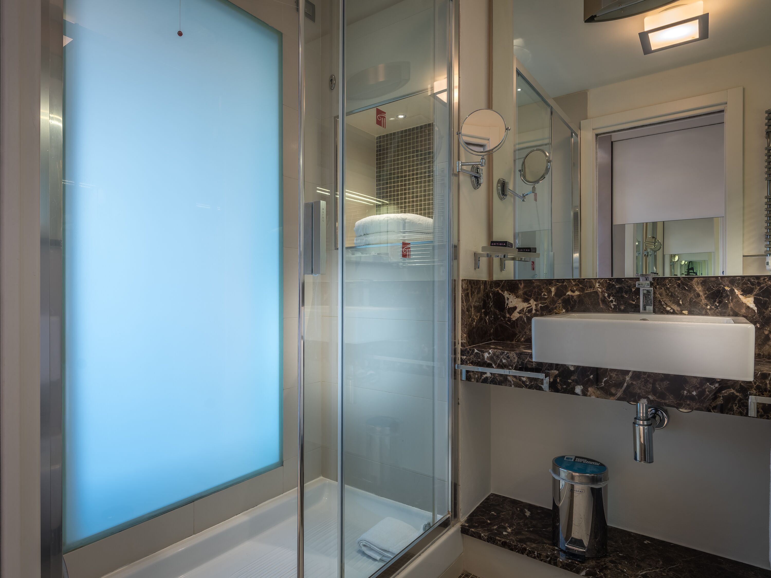 Un baño moderno con ducha de vidrio, encimera de mármol, lavabo y espejo.