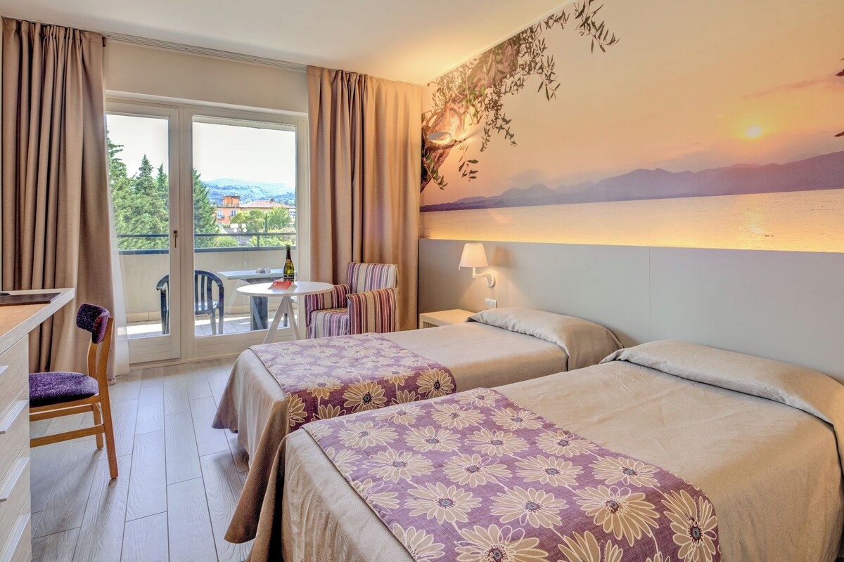 Ein Hotelzimmer mit zwei Betten, einem Schreibtisch, einem Stuhl und einem Balkon mit schöner Aussicht.