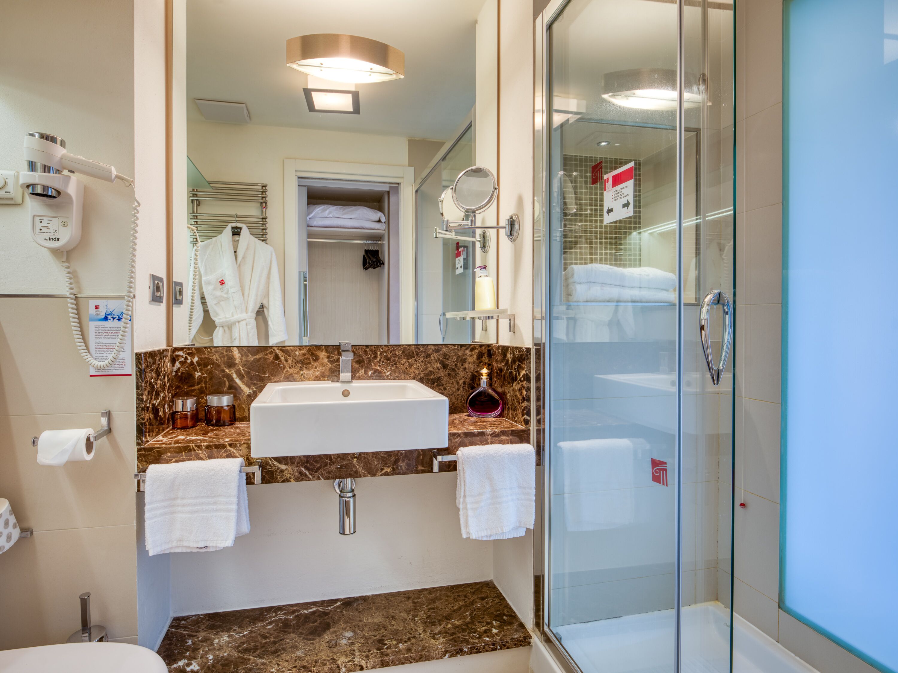 Une salle de bain moderne avec un comptoir en marbre, un lavabo, une douche en verre et un sèche-cheveux fixé au mur.