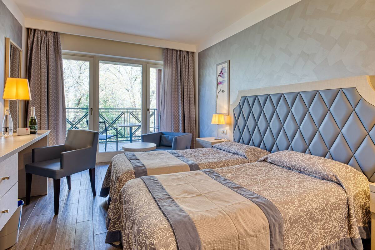Quarto de hotel com duas camas, uma escrivaninha e uma varanda.