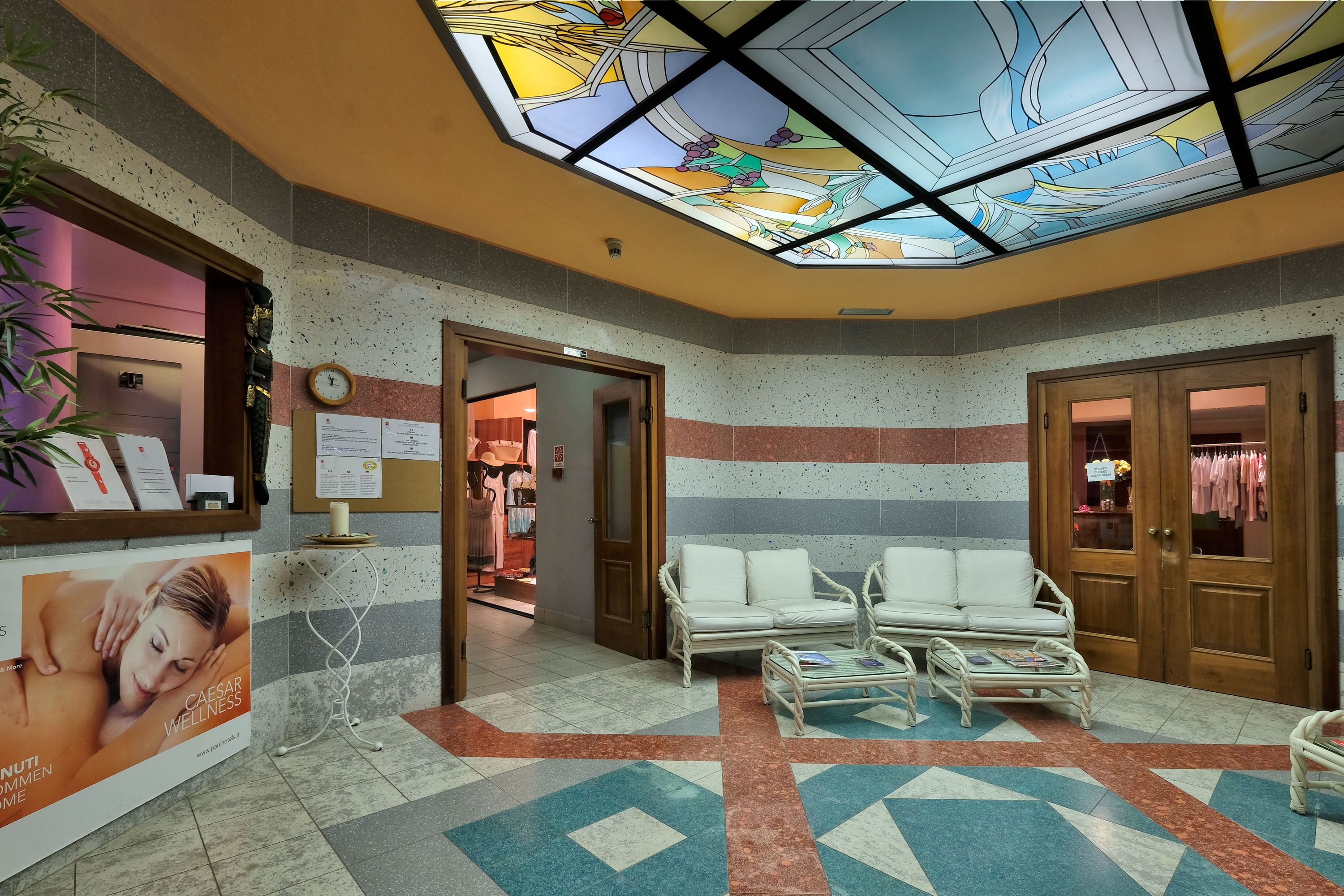 A lobby with a patterned floor, a white sofa, a small table, and a glass ceiling with a stained glass design.