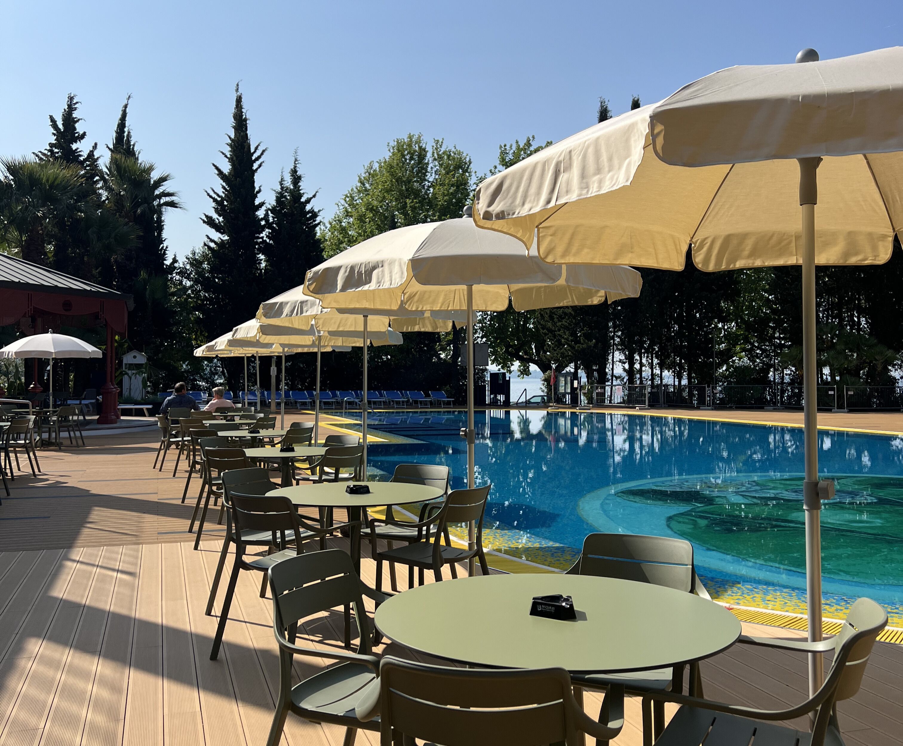 A poolside area with multiple tables and chairs, umbrellas, and a clear view of the pool.