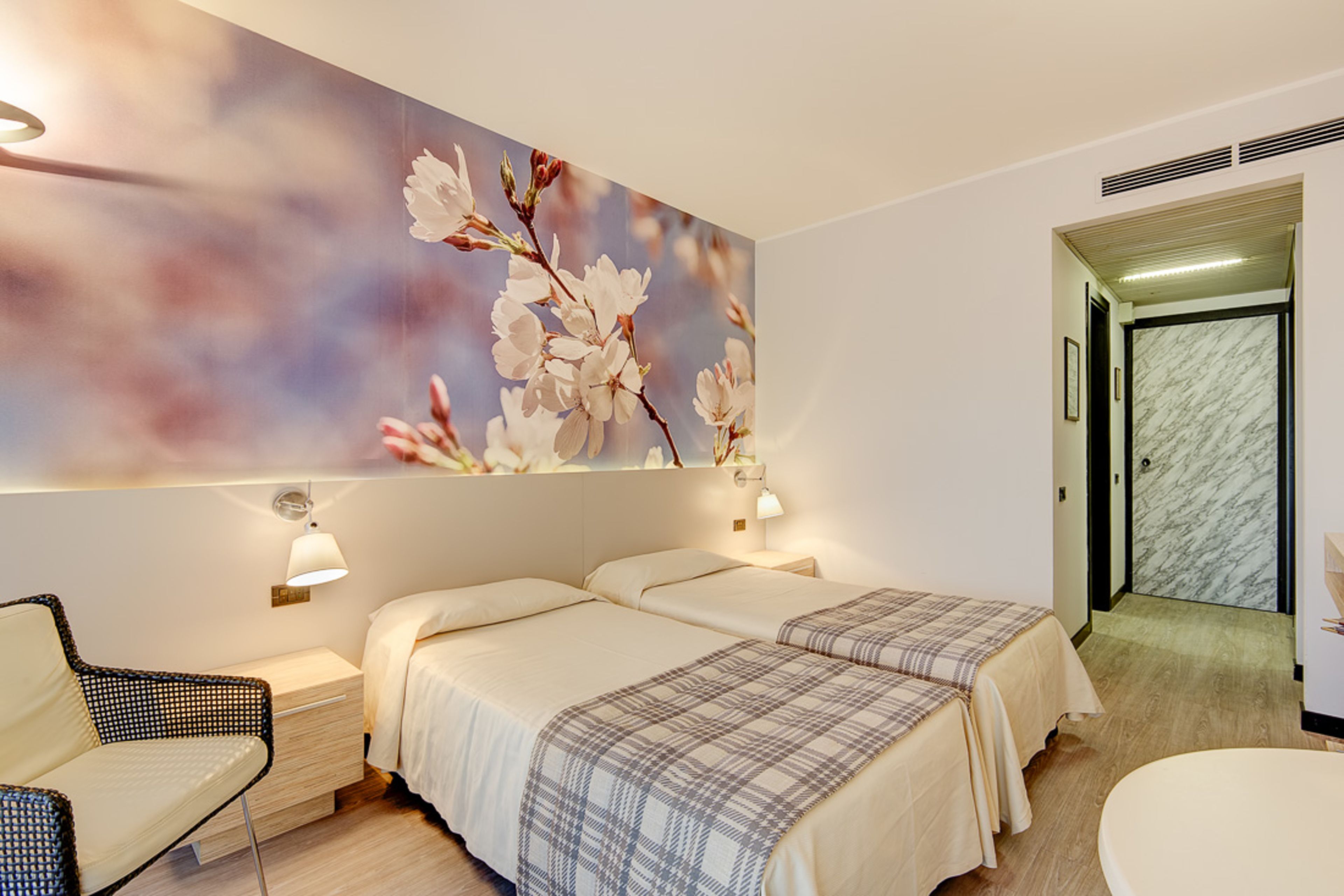 A hotel room with two beds, a nightstand, a chair, and a large floral mural on the wall.