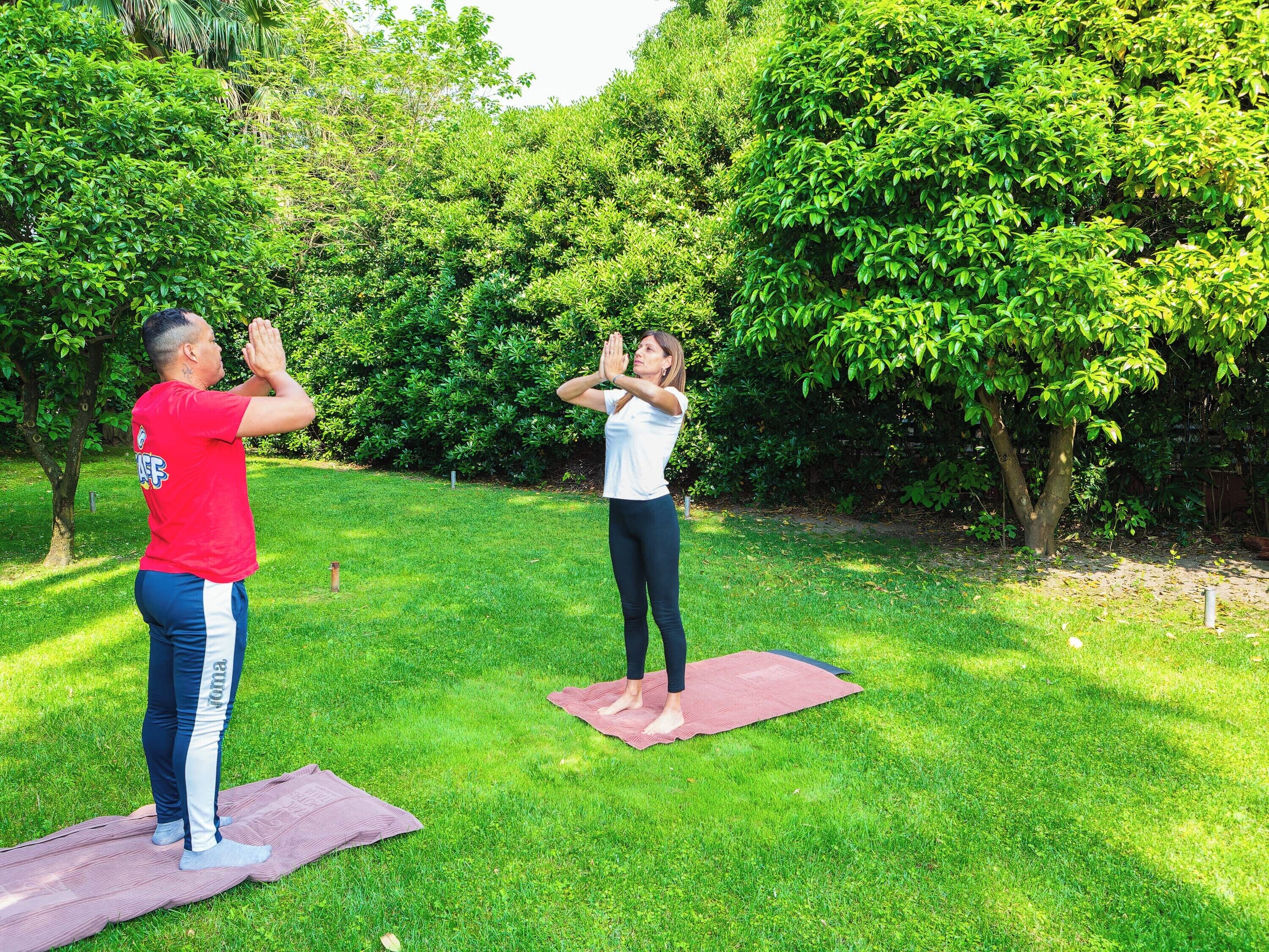 Two people practicing yoga outdoors on a grassy area with trees in the background.