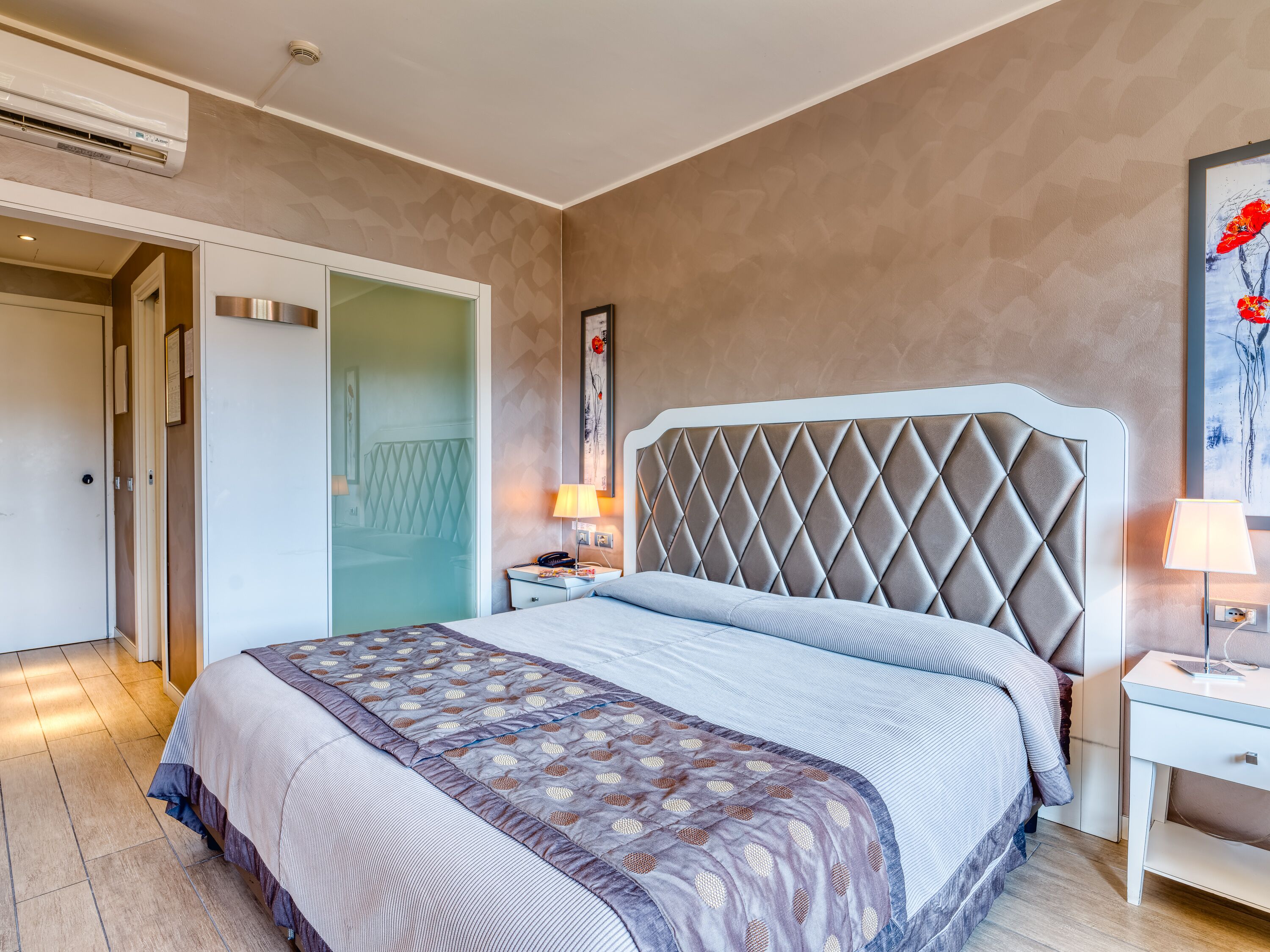 Een hotelkamer met een groot bed, nachtkastje, lamp en een schilderij aan de muur.