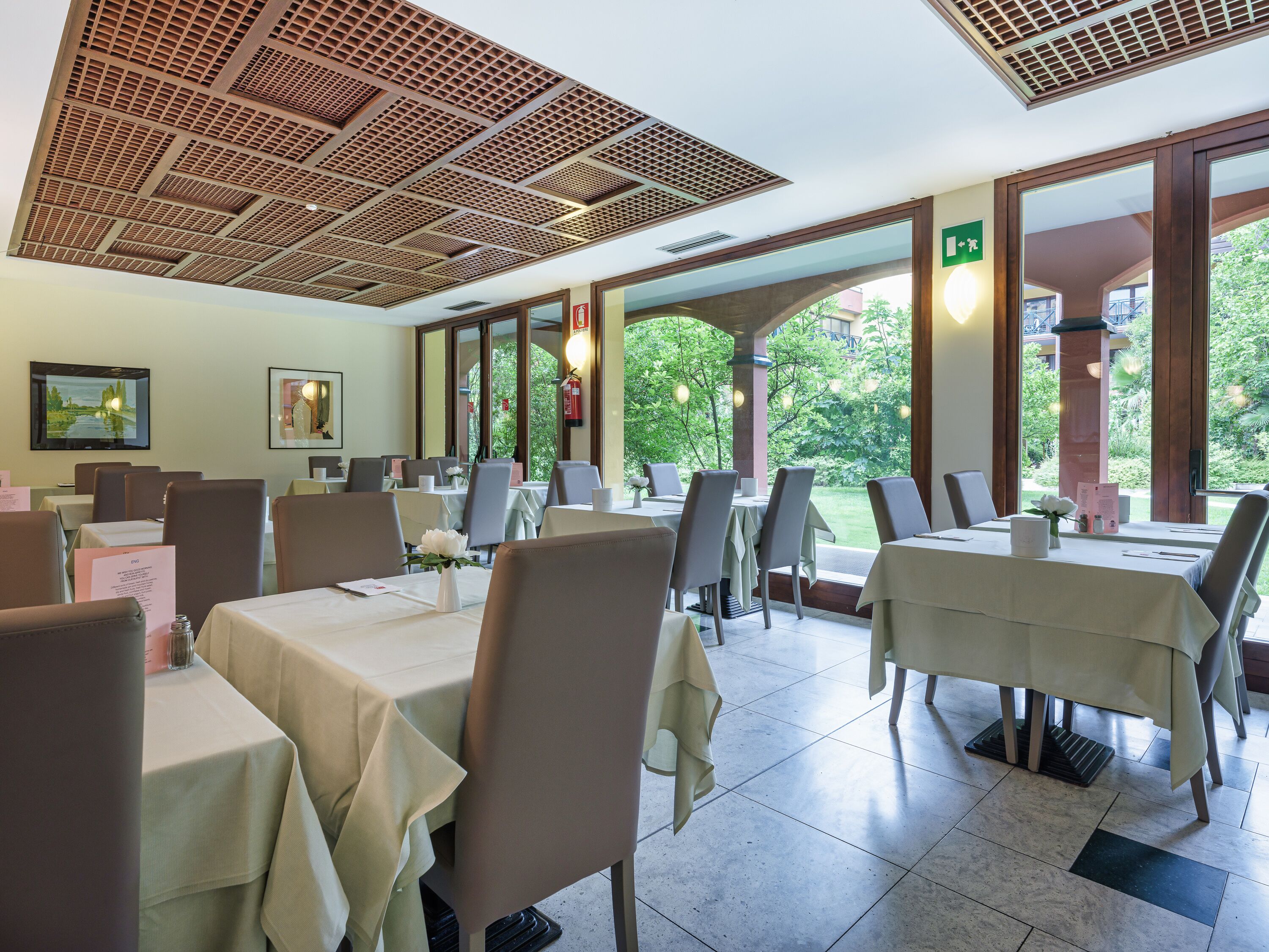 Un restaurante con varias mesas y sillas, amplias ventanas y un techo con diseño de cuadrícula.