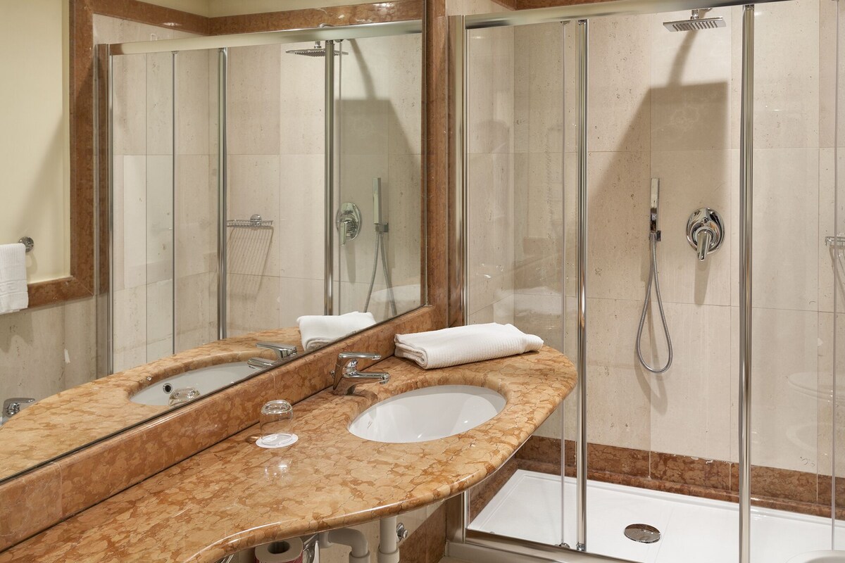 A modern bathroom with a marble vanity, a glass-enclosed shower, and a large mirror.