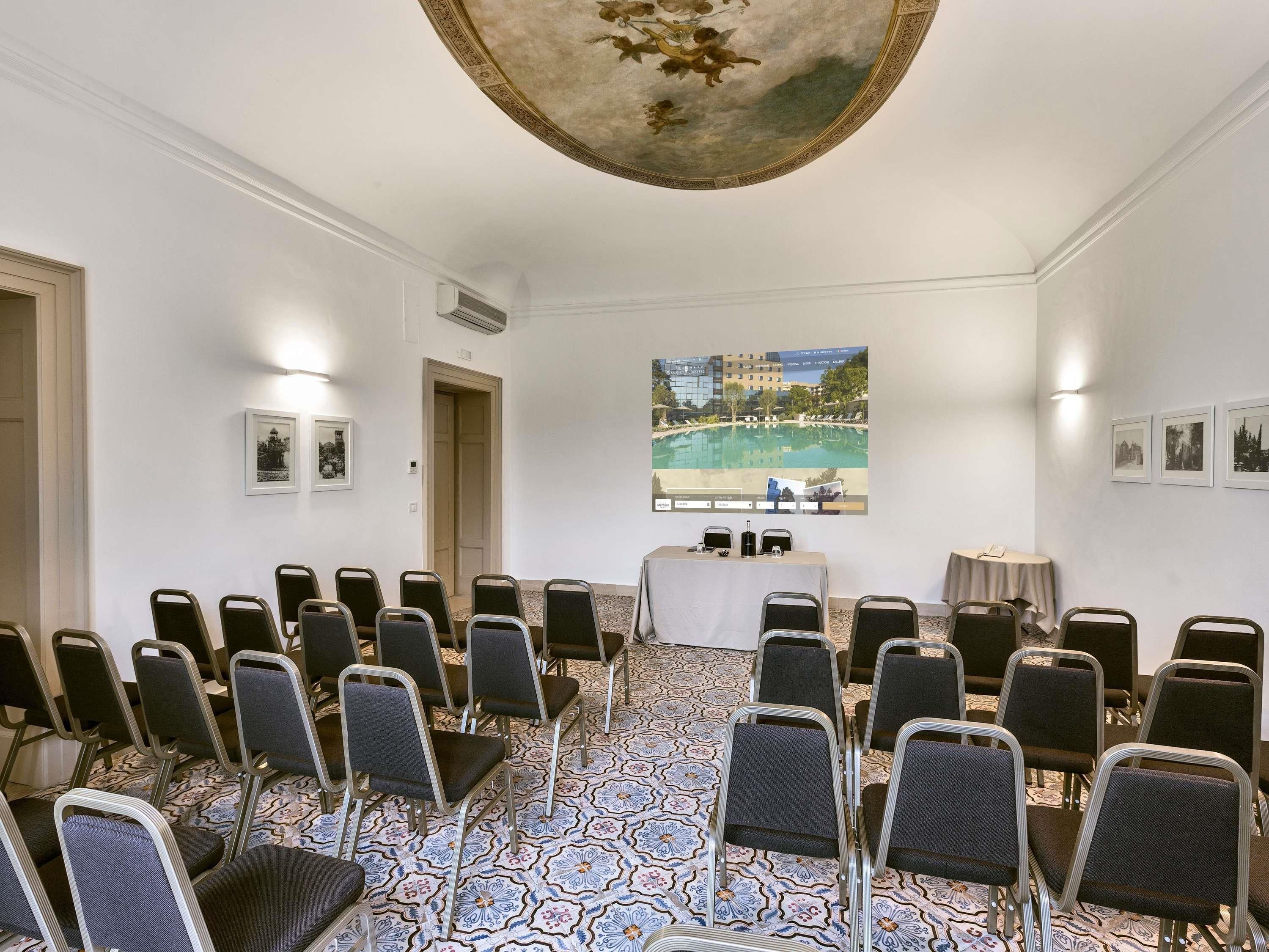 A conference room with rows of chairs, a table with a projector, and a large painting of a landscape.
