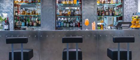 A bar area with three stools, shelves stocked with various liquor bottles, and a cash register.