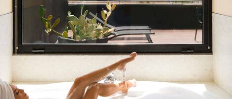 A bathtub with a city view, a window with a cactus plant, and a Samsung air conditioner.