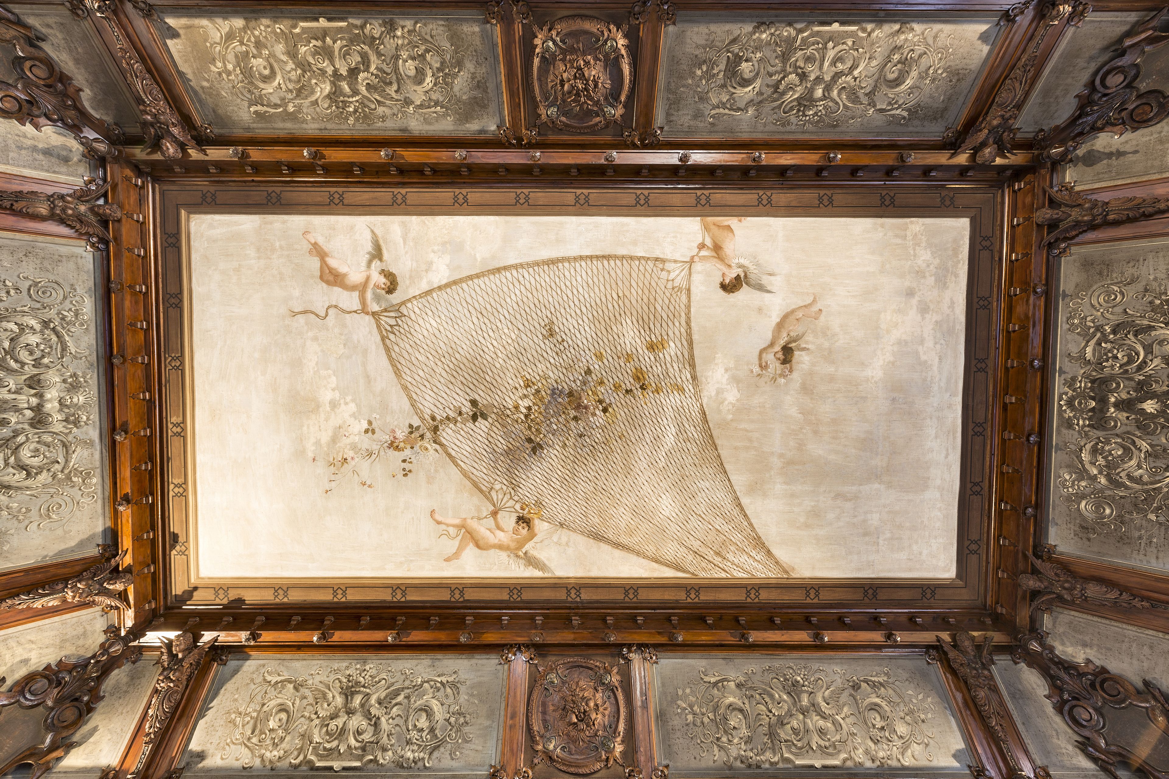 An ornate ceiling with intricate woodwork and a central fresco.