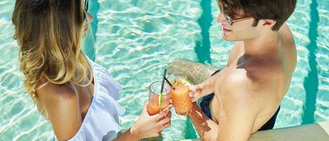 Two people at a poolside with drinks, a clear pool, and a concrete edge.