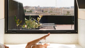 A bathtub with a city view, a window with a cactus plant, and a Samsung air conditioner. - Mercure Villa Romanazzi Carducci Bari (Bari)