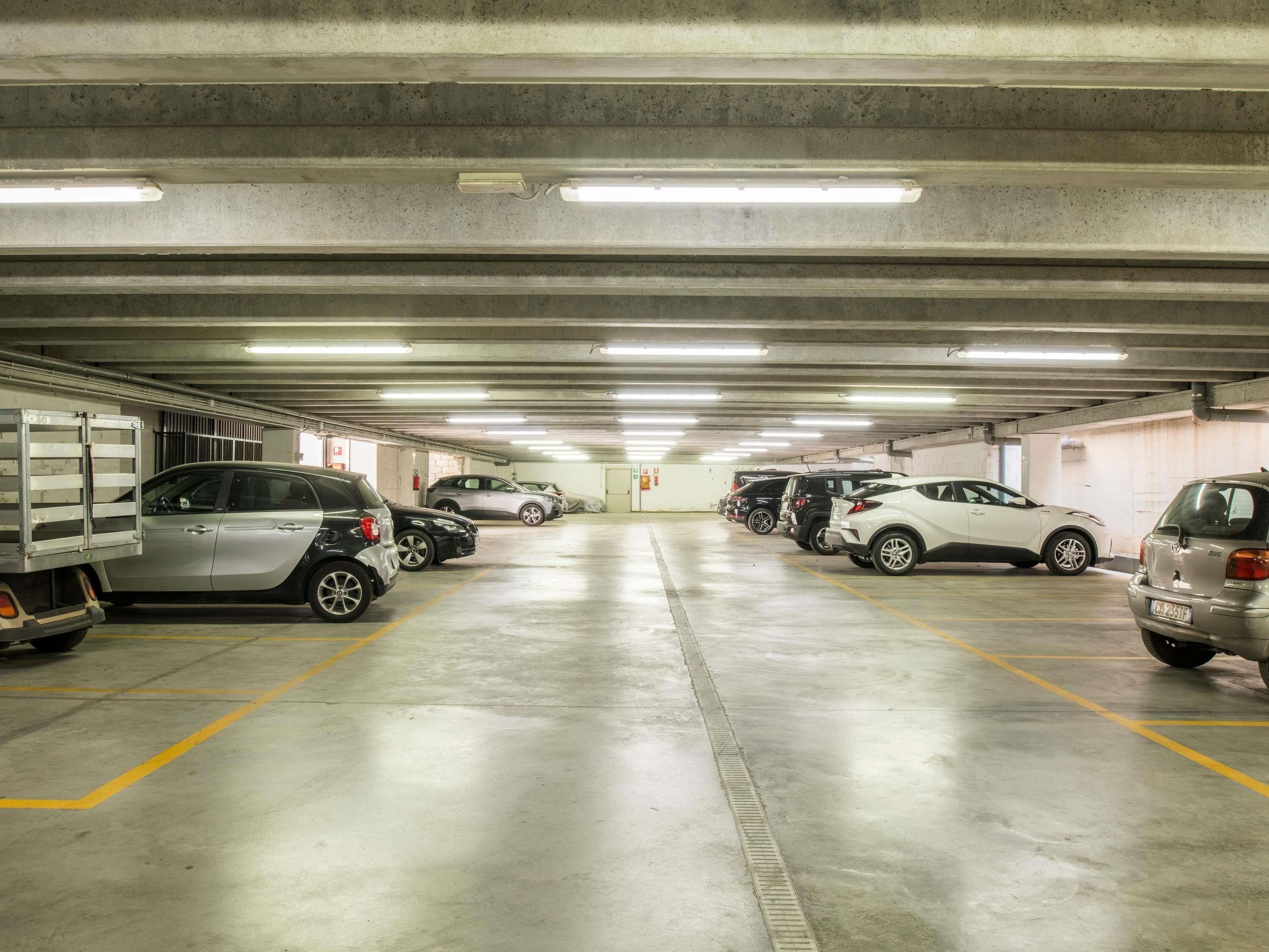 A multi-level underground parking garage with several cars parked in rows, concrete walls, and overhead fluorescent lighting.