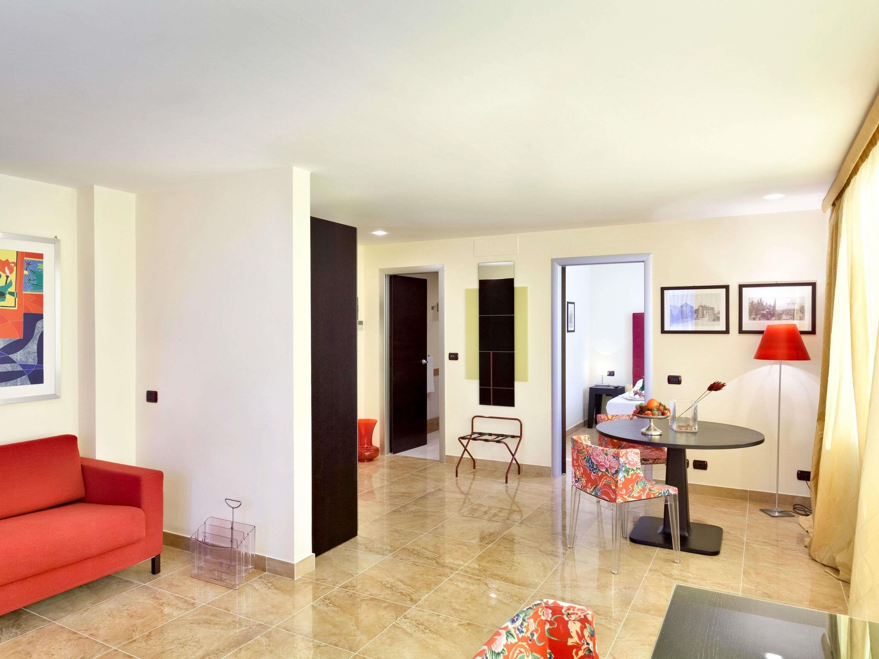 A modern living room with a red sofa, a dining area with a round table and chairs, and a kitchen visible in the background.